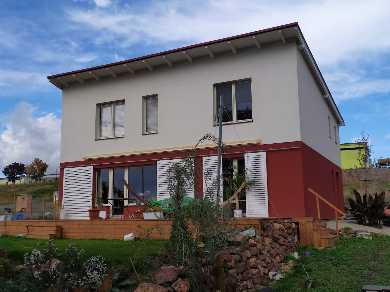 Grau-rotes Haus mit Pultdach, Terrasse und angelegter Bepflanzung